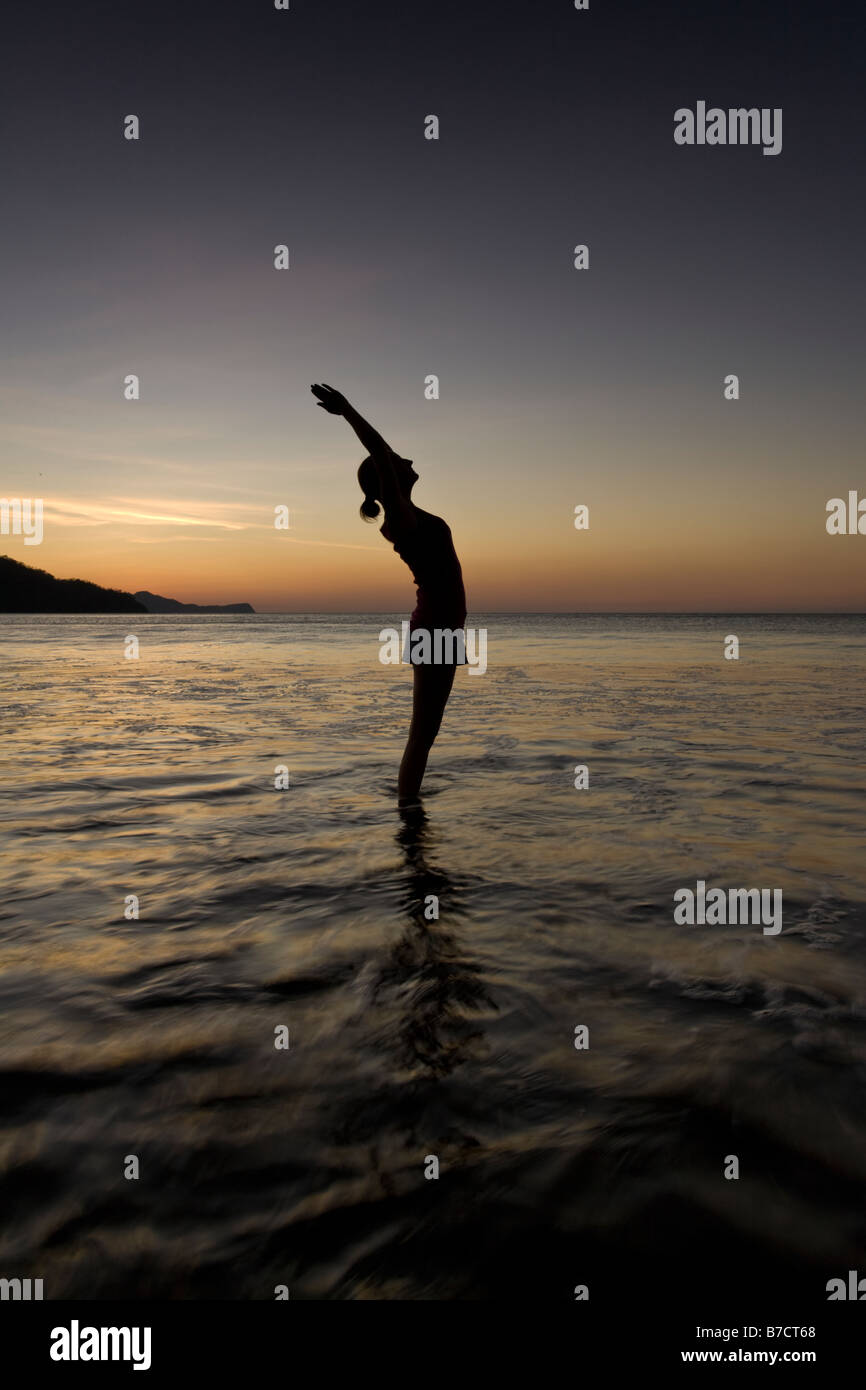 Silhouette of young woman doing yoga at the beach during sunset in ...
