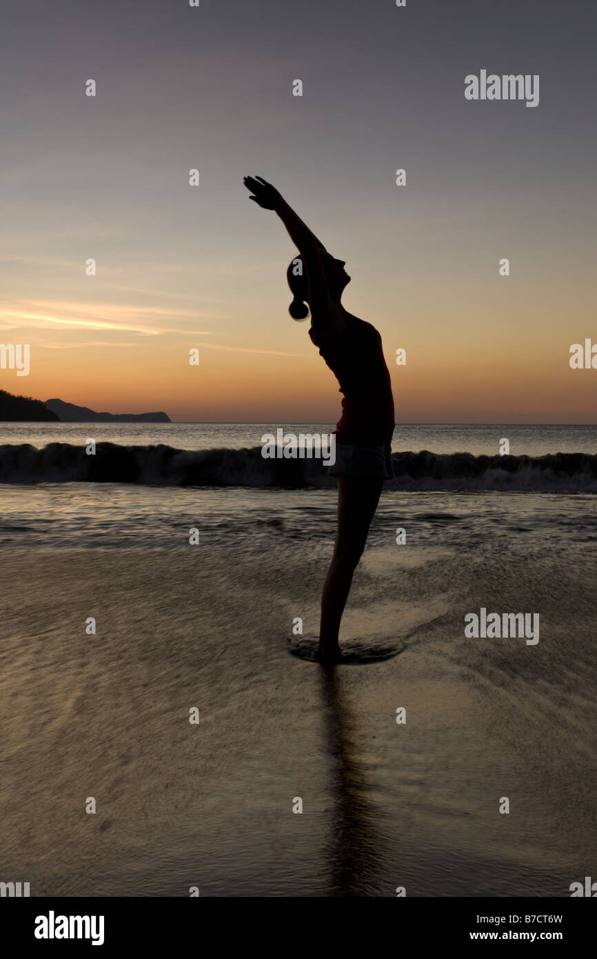 Silhouette of young woman doing yoga at the beach during sunset in Playas del Coco, Costa Rica. Stock Photo