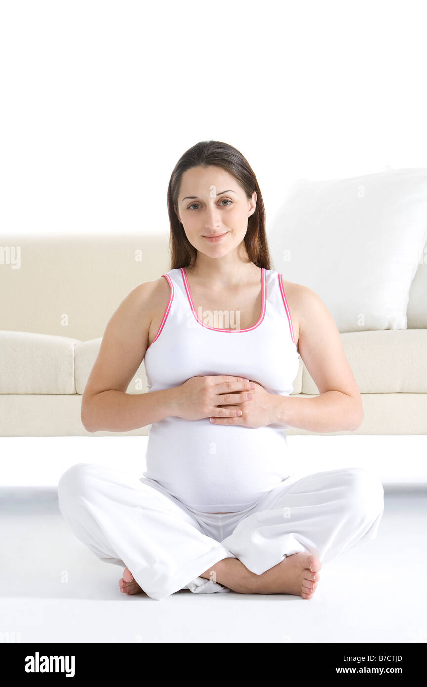 Pregnant young woman sitting cross legged in front of a sofa hands