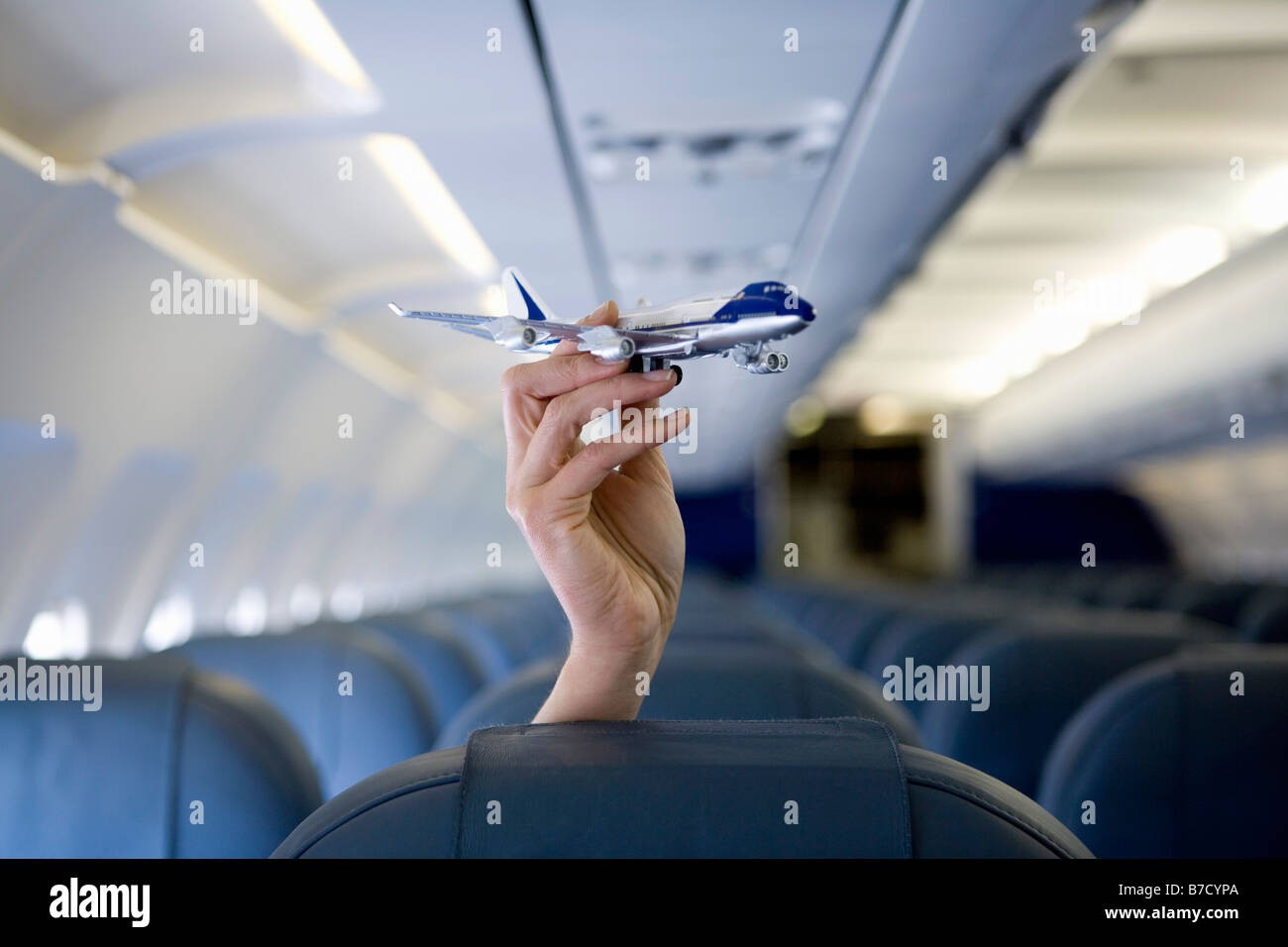 A hand holding a toy airplane above an airplane seat Stock Photo