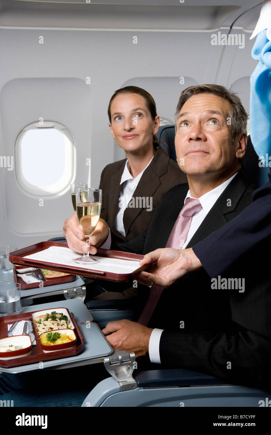 Business people on a plane being served meals and champagne Stock Photo