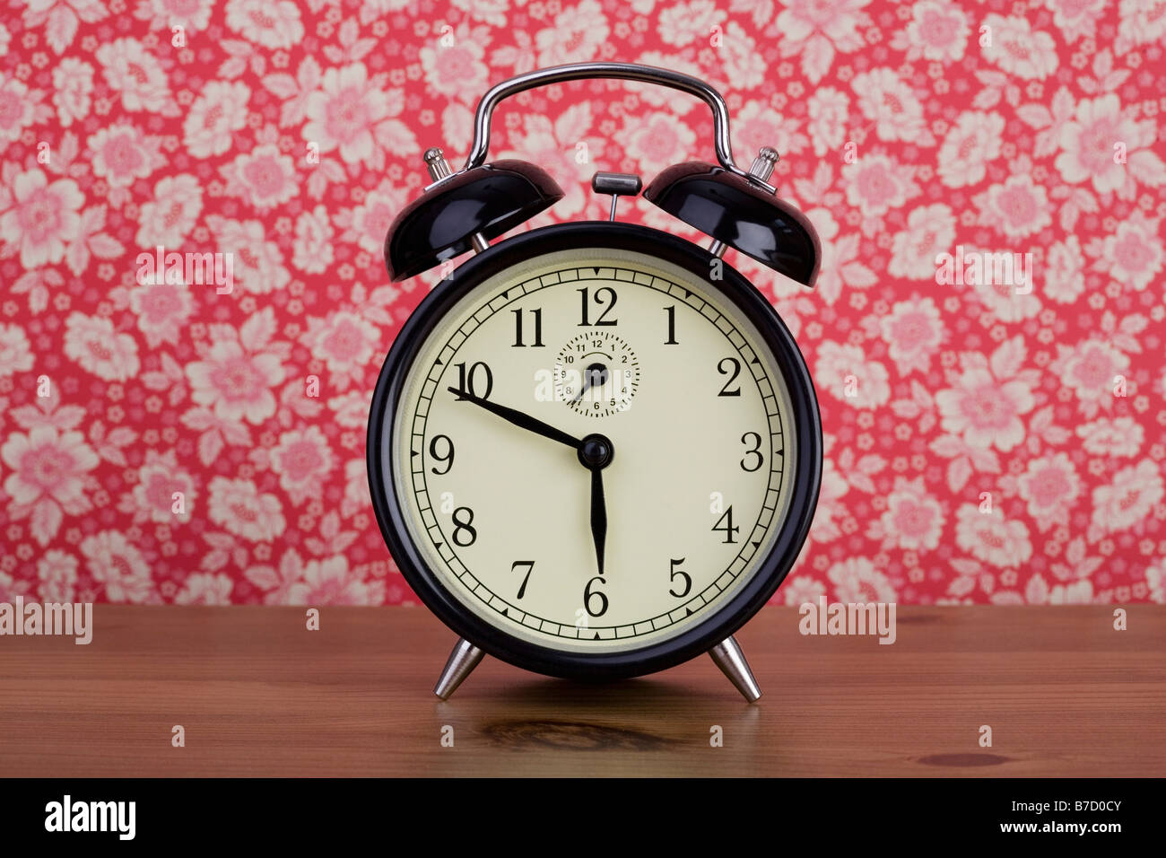 An old fashioned alarm clock in front of floral patterned wallpaper Stock Photo Alamy