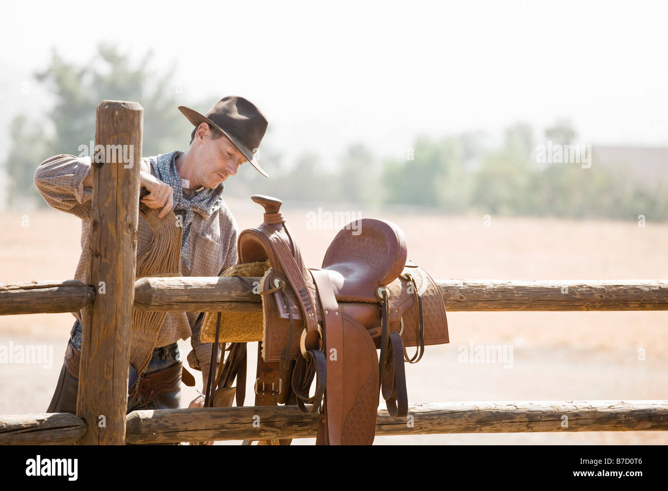 A rancher preparing a horse saddle on a fence Stock Photo
