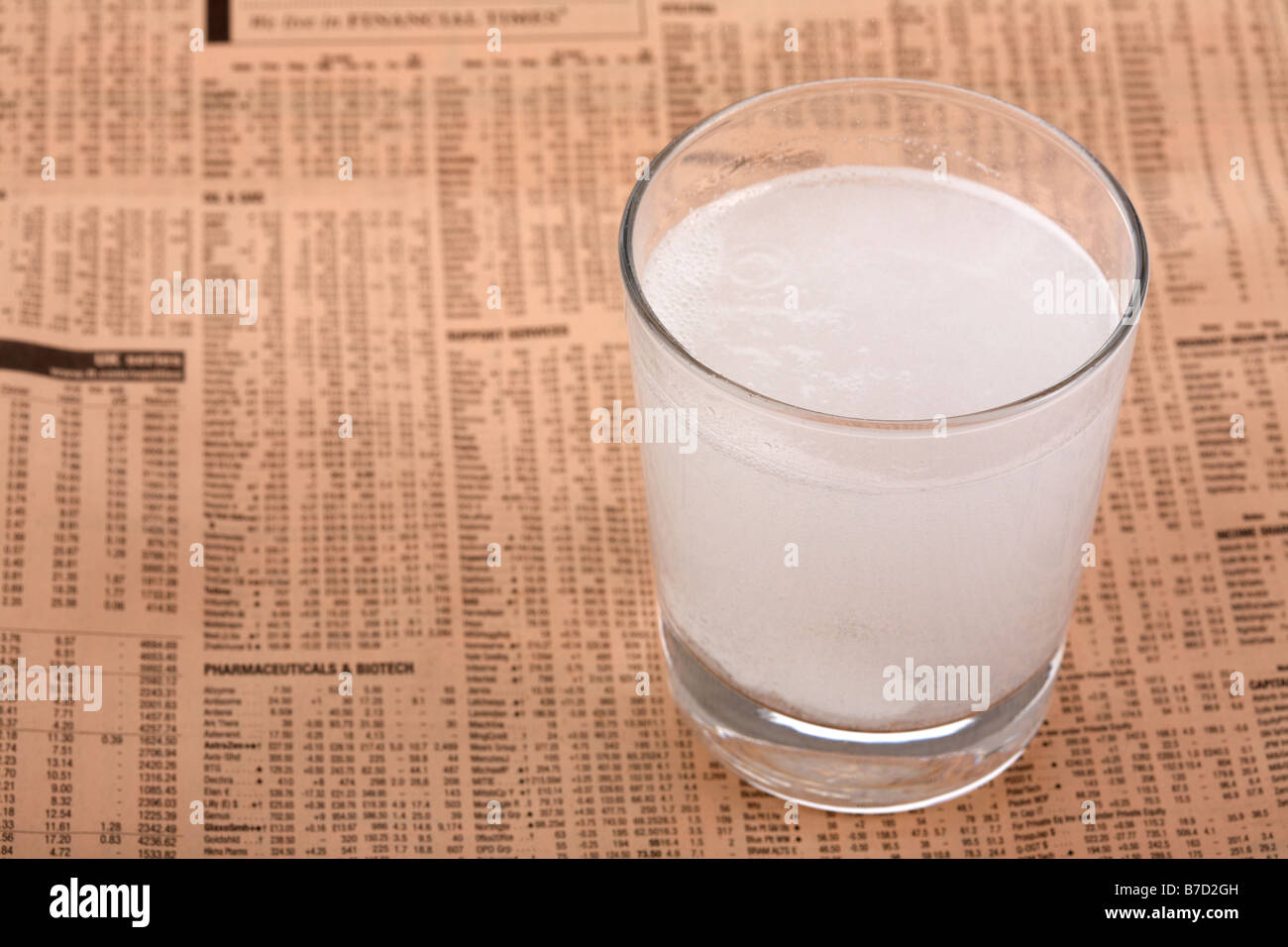 two soluble paracetamol aspirin tablets in a glass of water on a copy of the financial times Stock Photo
