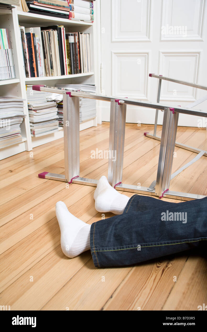 Human legs lying next to a ladder on its side Stock Photo