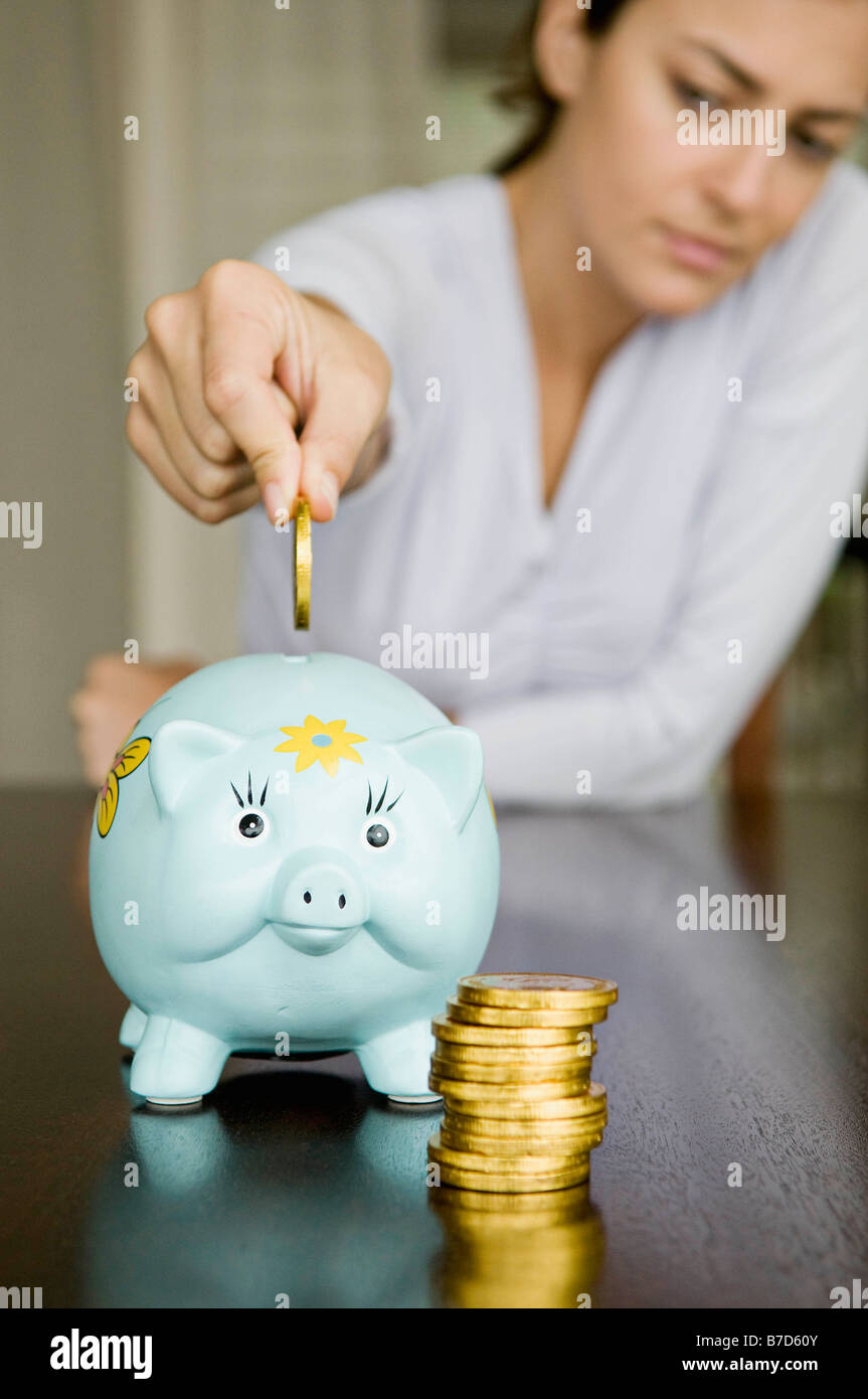 Woman dropping money into a piggy bank Stock Photo - Alamy