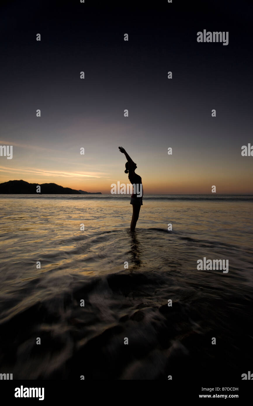 Silhouette of young woman doing yoga at the beach during sunset in ...