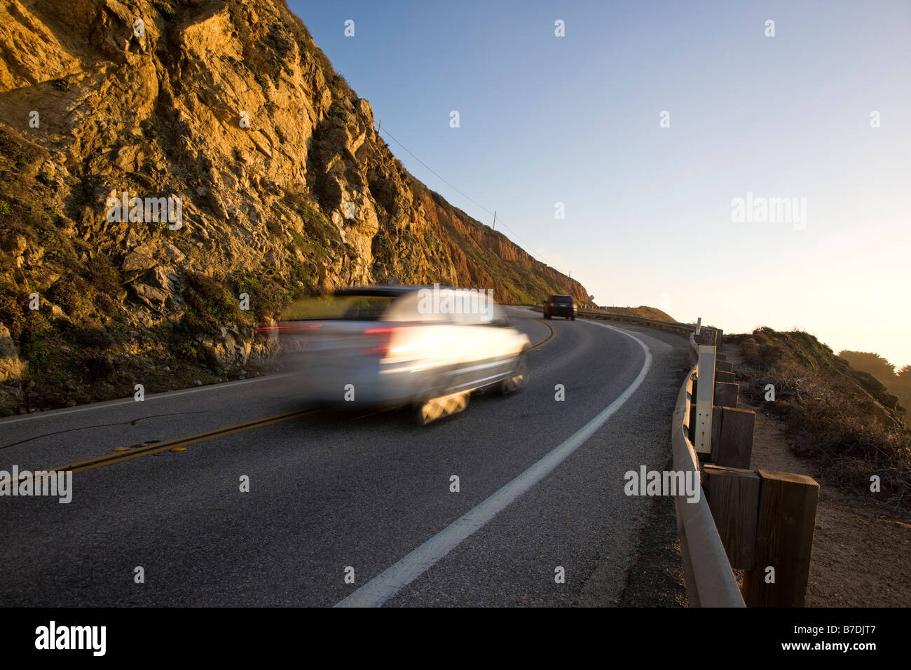 Speeding car in a blur of motion on highway 1 at sunset north of the Bixby Bridge, Big Sur, California, USA Stock Photo