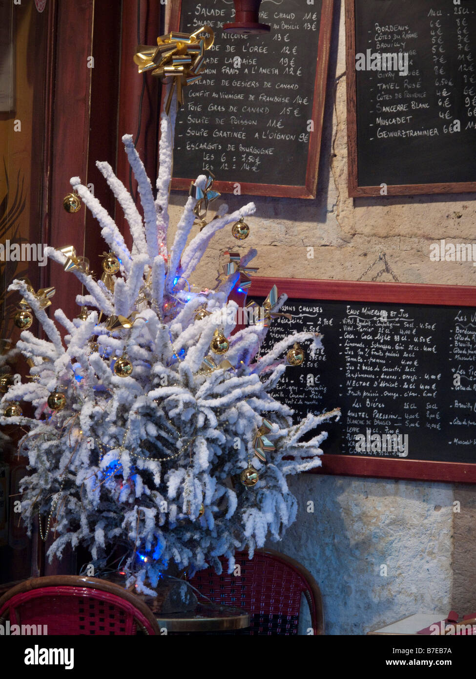 Small white decorated Christmas tree sits on a table in a Paris, France cafe in front of menu boards written in chalk. Stock Photo