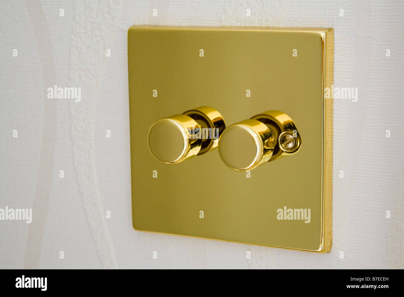 Gold metal double electric dimmer light switch on a wall. England UK Britain Stock Photo