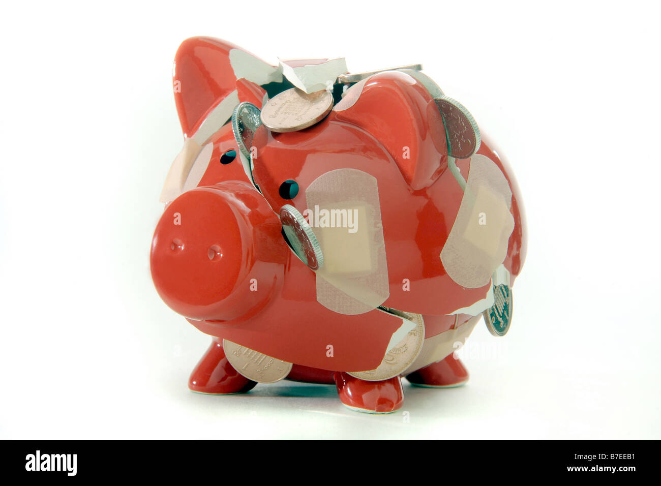A BROKEN RED PIGGYBANK LOSING ITS CONTENTS OF BRITISH COINS... HELD TOGETHER WITH PLASTERS. Stock Photo