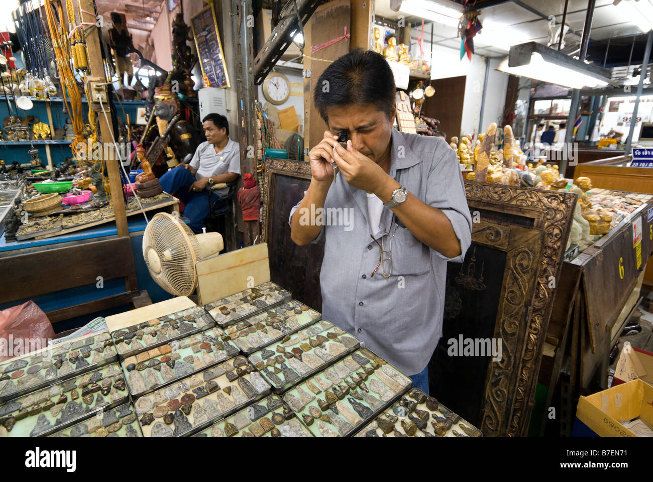 Collector searching through small Buddhist amulets on a stall in Amulet Alley market in Phra Nakorn area Bangkok Thailand Stock Photo