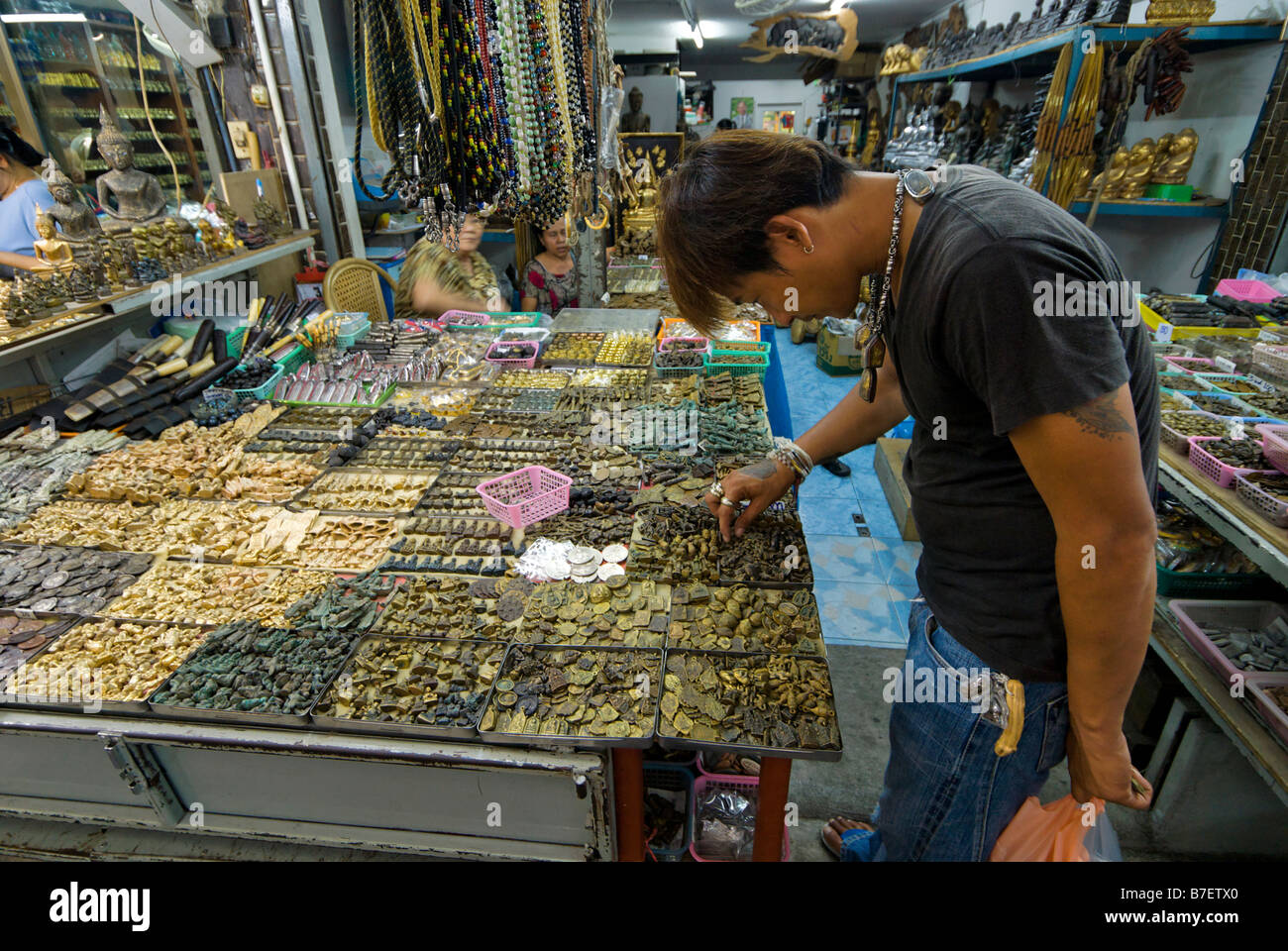 Collector searching through small Buddhist amulets on a stall in Amulet Alley market in Phra Nakorn area Bangkok Thailand Stock Photo