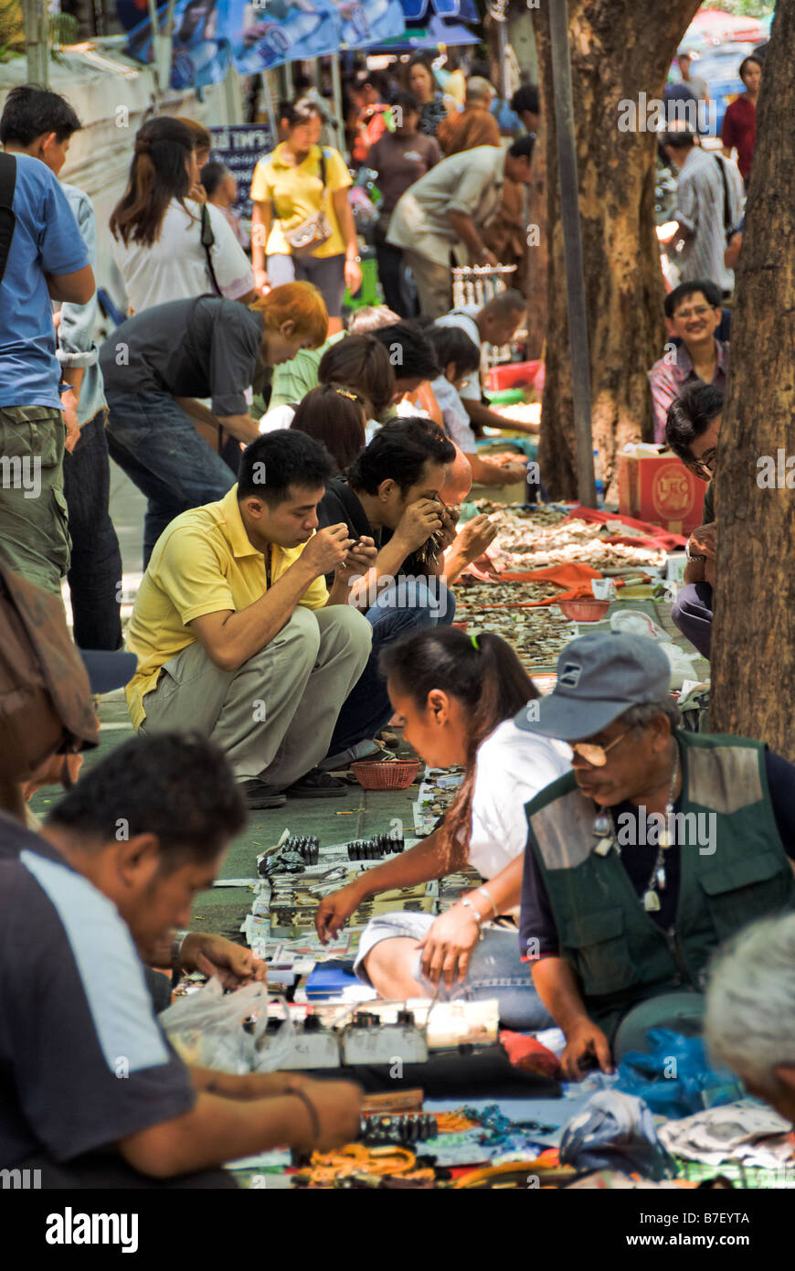 Collectors searching through small Buddhist amulets in in the street near Amulet Alley market - Bangkok Thailand Stock Photo
