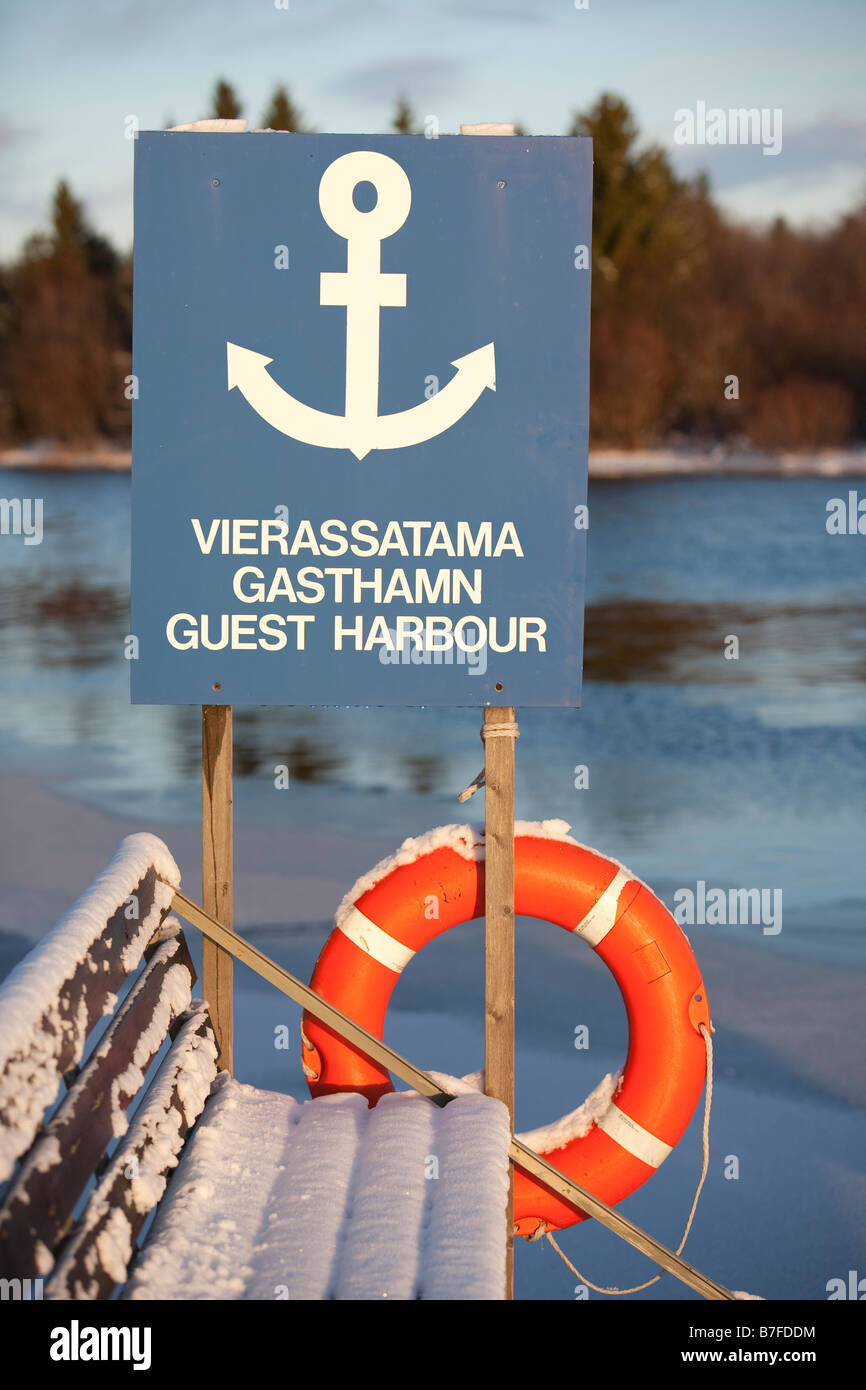 Snowy wooden bench and guest harbour sign ( in Finnish , Swedish  and English ) at small boat's harbor, Finland Stock Photo