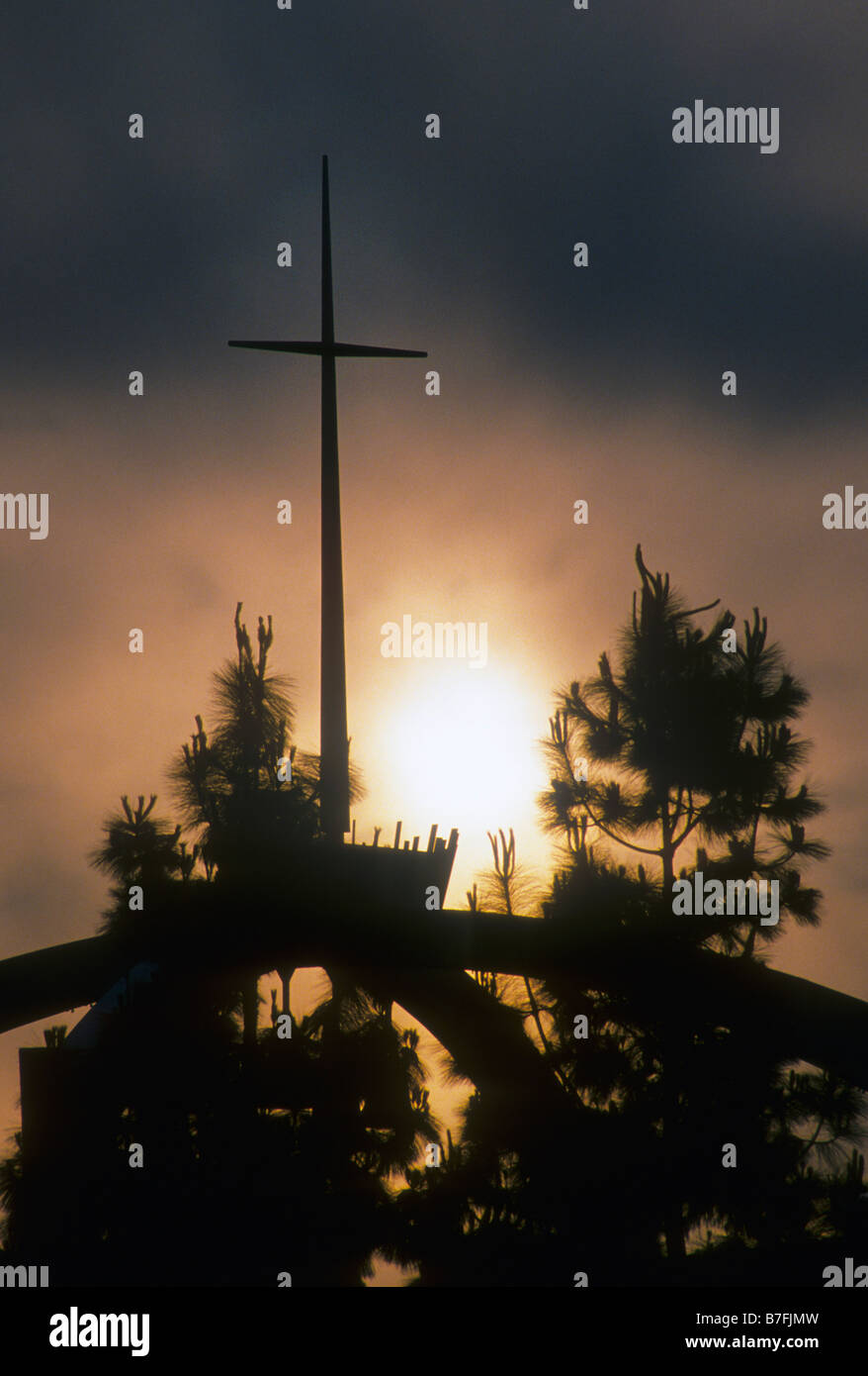 Cross on top of church stands out against glowing sunset sky Stock