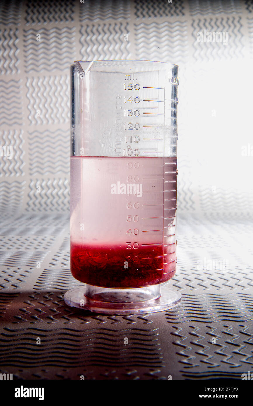 Beaker containing 100 ml of clear liquid solution and large amount of undissolved solids at bottom of beaker Stock Photo