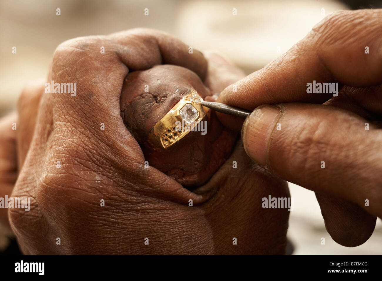 Goldsmith working on an unfinished 22 carat gold ring with his hard working hands Half of the Diamonds already embedded Stock Photo