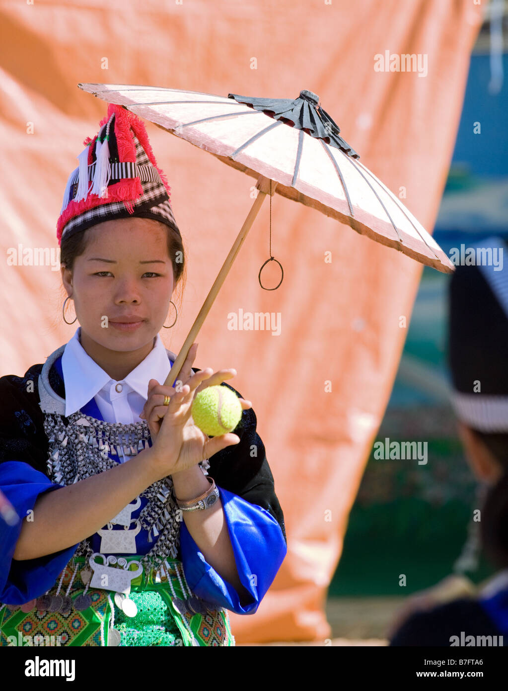A Hmong woman in traditional costume catches a ball under the shade of her parasol at a Hmong New Year celebration. Stock Photo