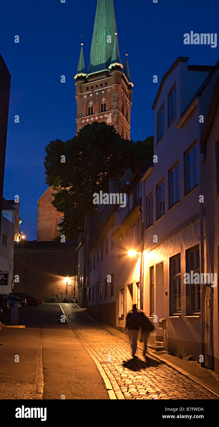 Blurred figures walking at night in cobbled street with gas lighting Lubeck Germany Stock Photo