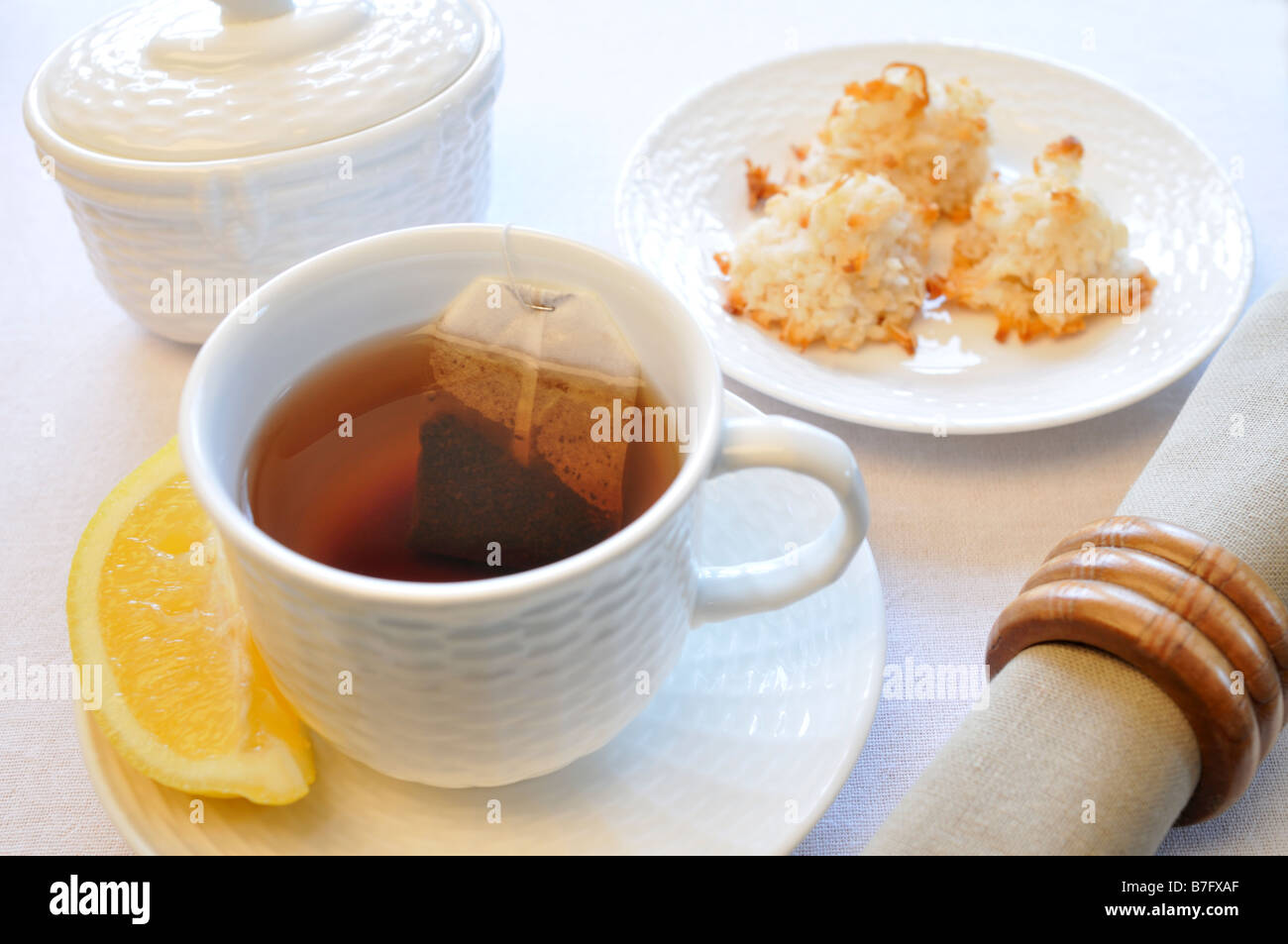 Black tea in cup with lemon coconut macaroon cookies napkin and sugar bowl on table Stock Photo