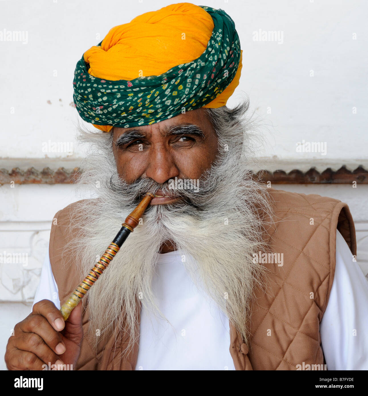 A roguish man with long grey whiskers, beard and moustache and an orange turban poses for tourists Stock Photo