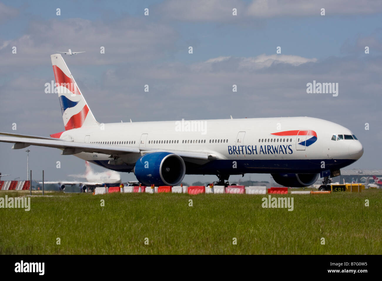 British Airways Boeing 777-236/ER and another commercial airplane taking off in the background at London Heathrow airport. Stock Photo