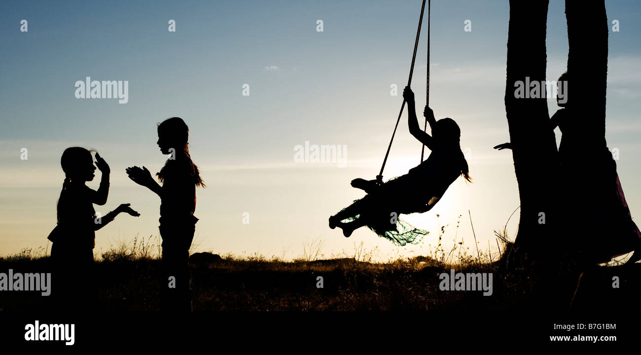 Silhouette of Indian girls swinging and hand clapping in the rural Indian countryside at sunset. Andhra Pradesh, India. Panoramic Stock Photo