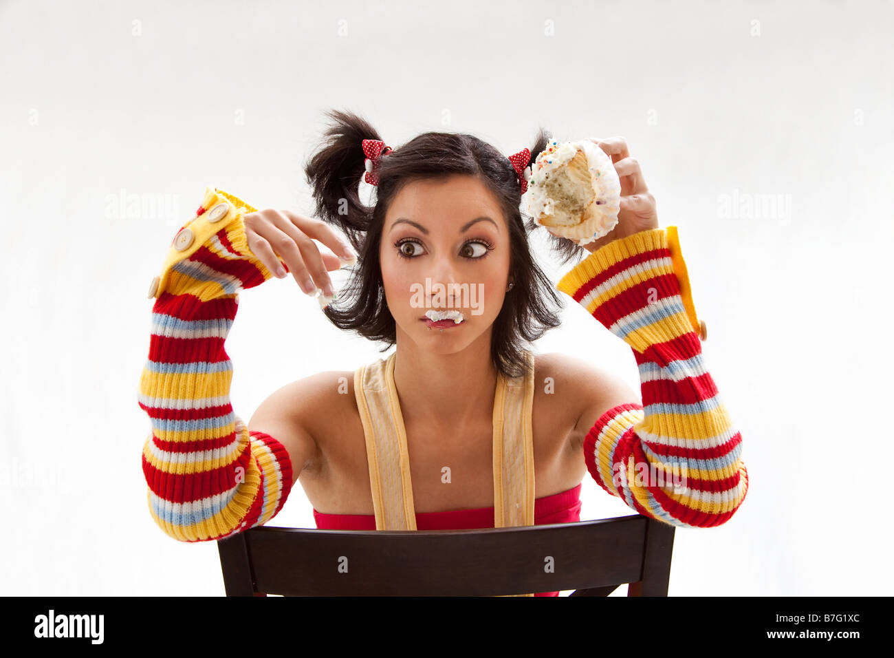 Beautiful Latina girl eating a cupcake with her fingers looking cross eyed isolated Stock Photo