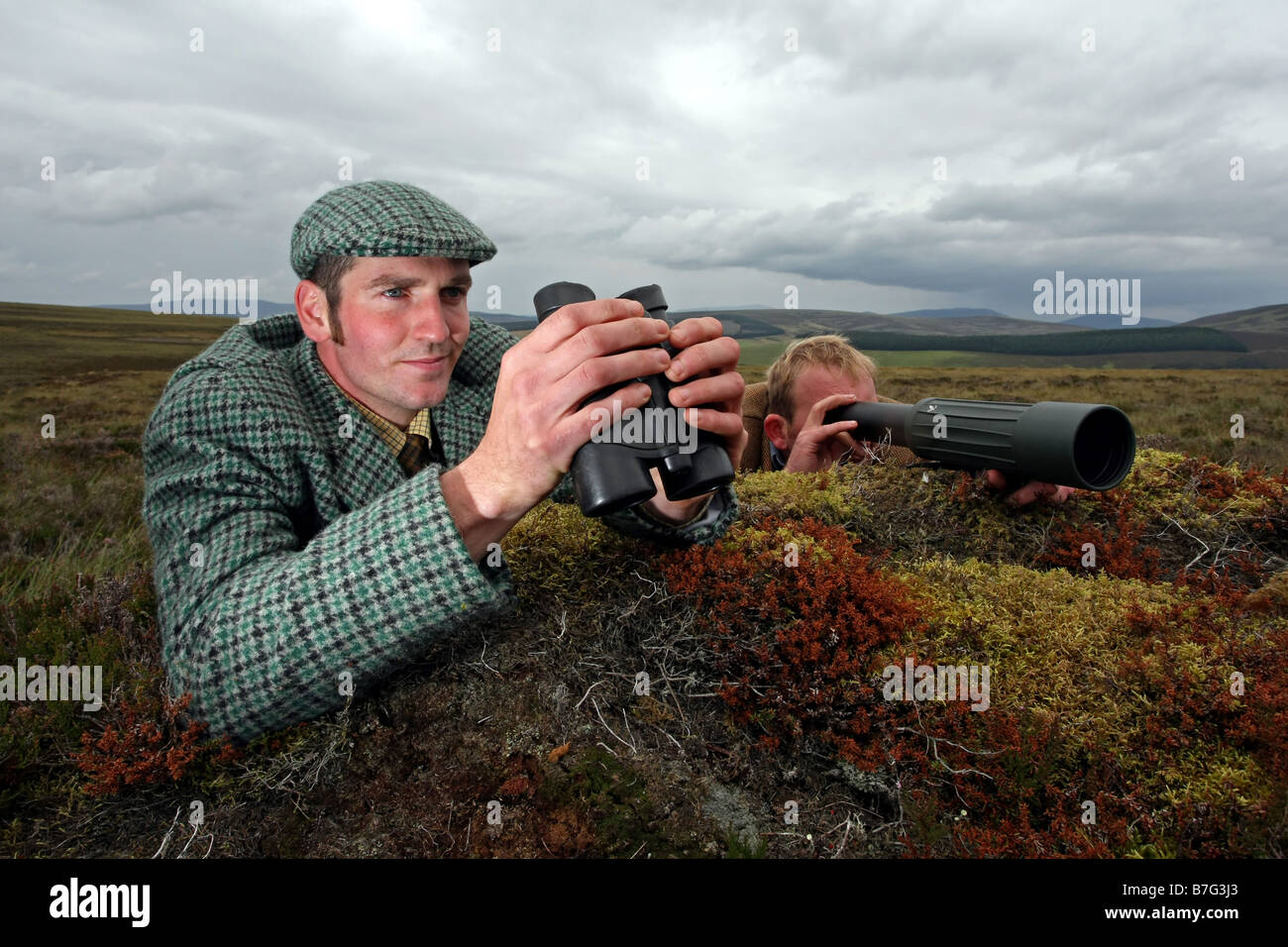 Stalkers using binoculars and telescope to spot deer on hills in Scotland, UK Stock Photo