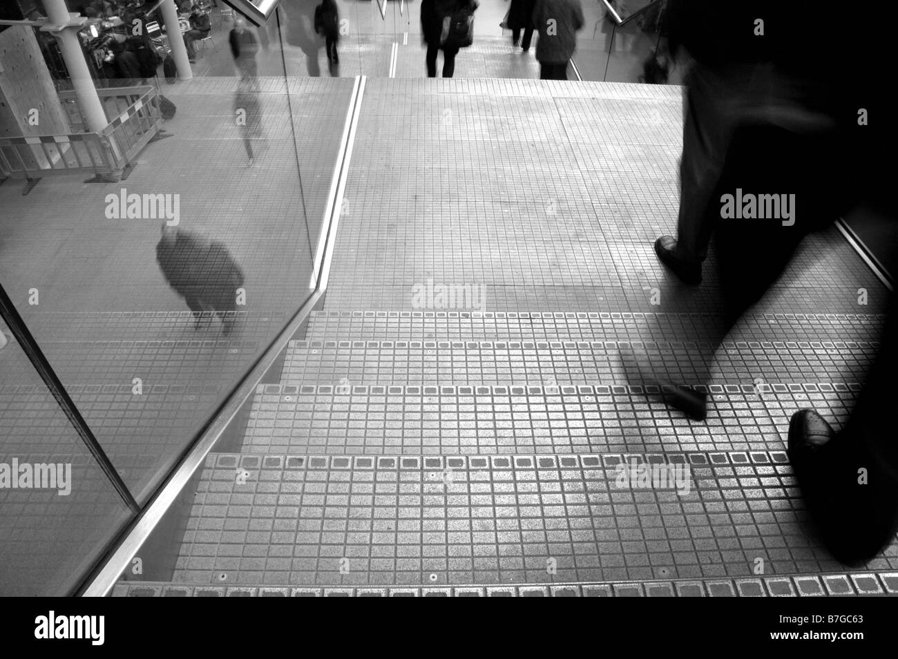 Black and white image of a man's legs and feet walking down stairs in blurred motion with people walking on pavement below. Stock Photo