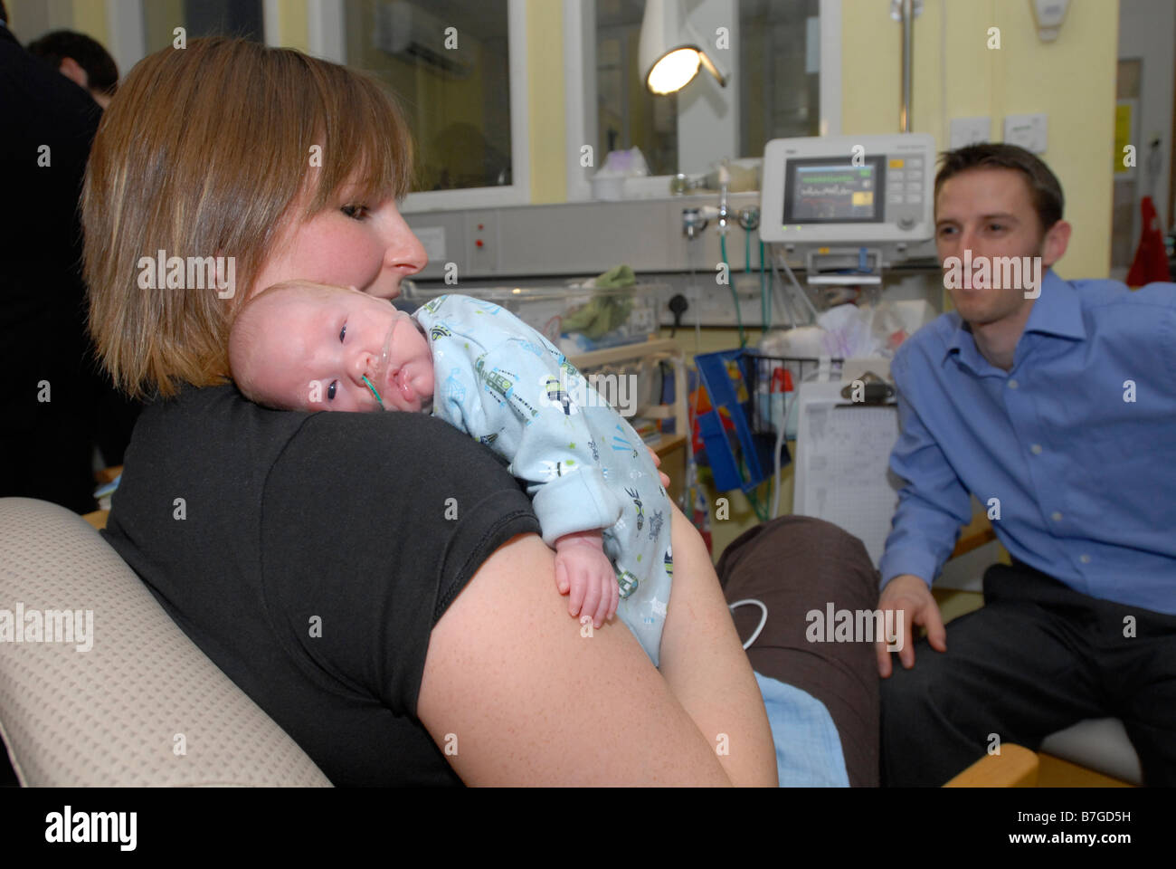 Mum holds her premature baby with Dad looking on Stock Photo