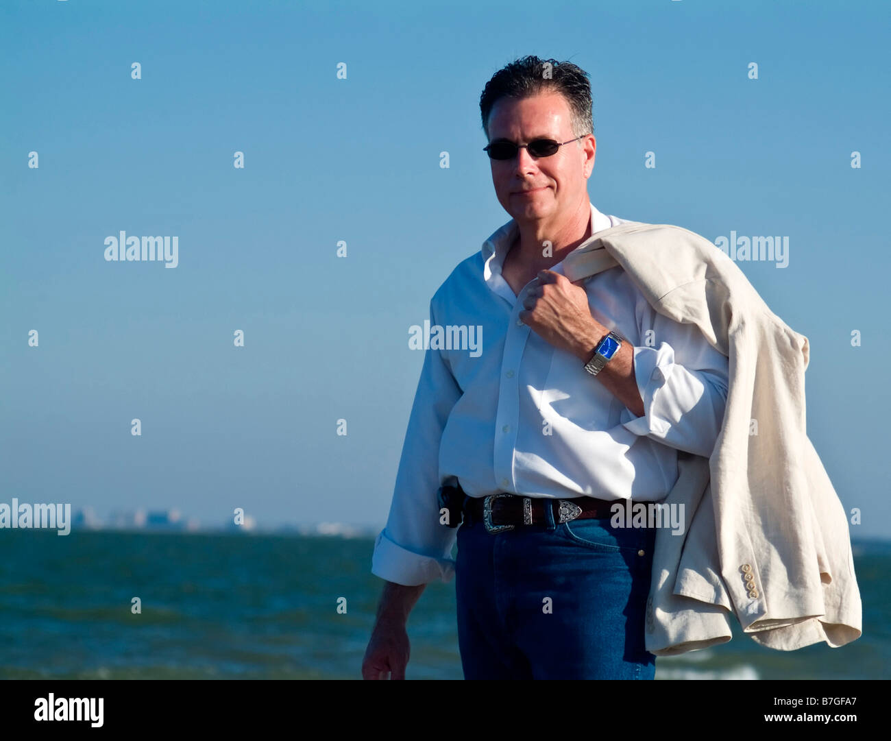 A man with sunglasses lit by late afternoon light with water and building in the background Stock Photo