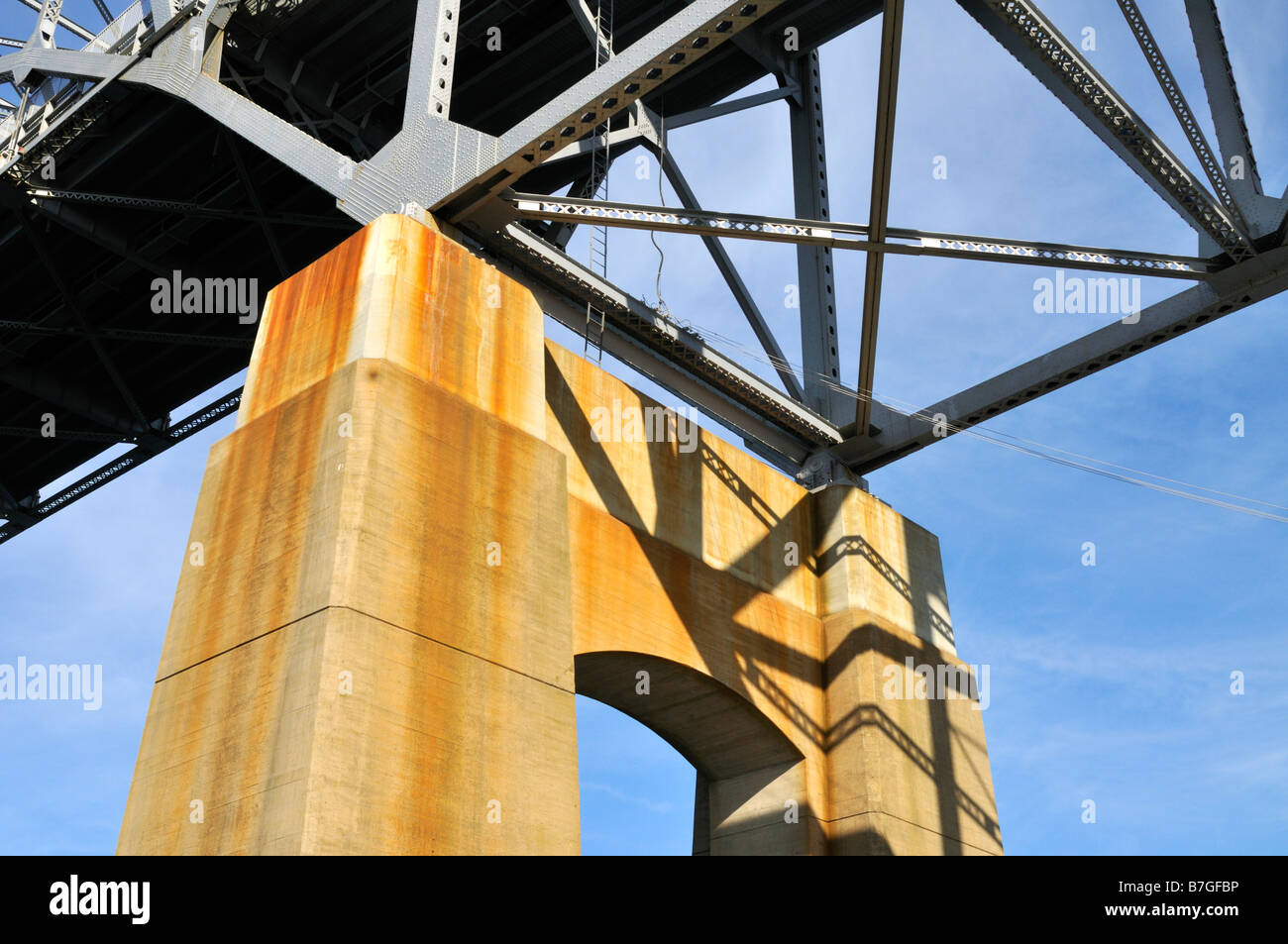 Looking up from under a bridge showing the concrete support steel girders and blue sky Stock Photo