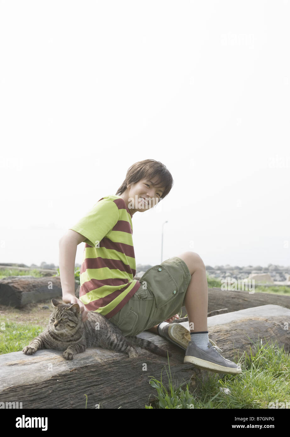 Smiling boy with cat sitting on the lying tree in the field Stock Photo ...