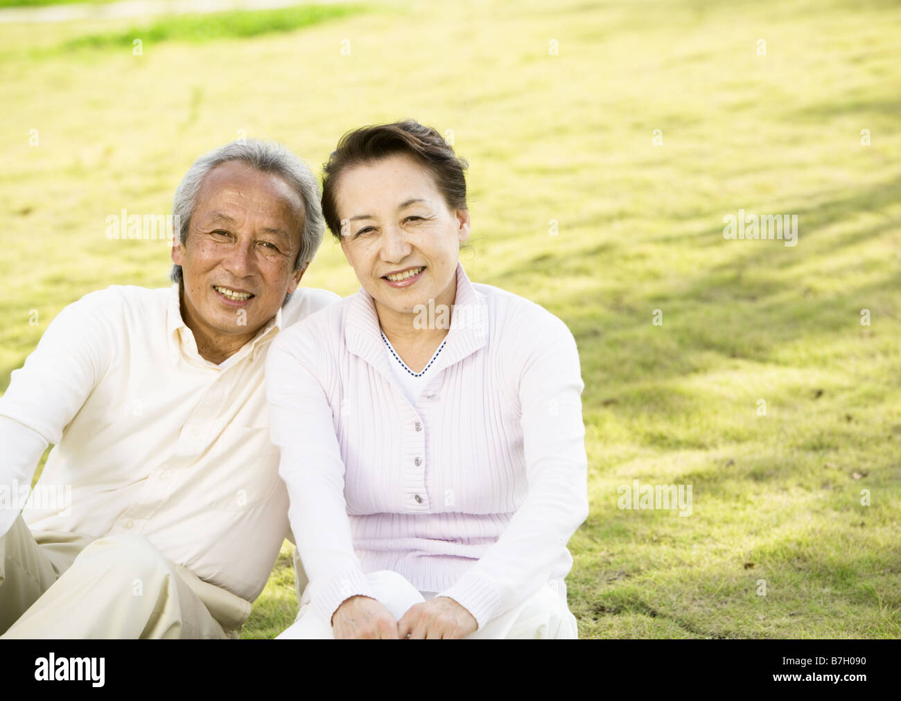 Elderly couple sitting in garden, smiling Stock Photo. 