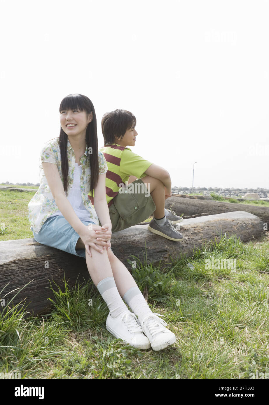 Smiling boy and girl sitting on the lying tree in the field Stock Photo ...