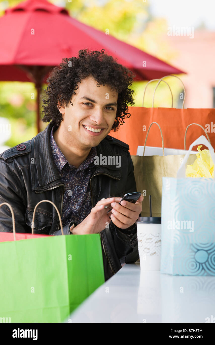 Middle Eastern man with shopping bags text messaging on cell phone Stock Photo