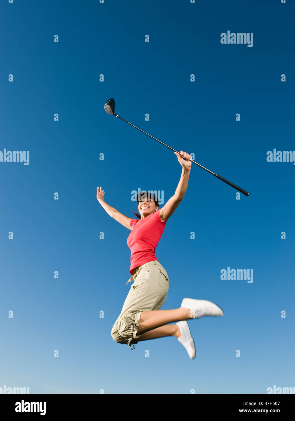 Native American woman with golf club jumping in mid-air Stock Photo