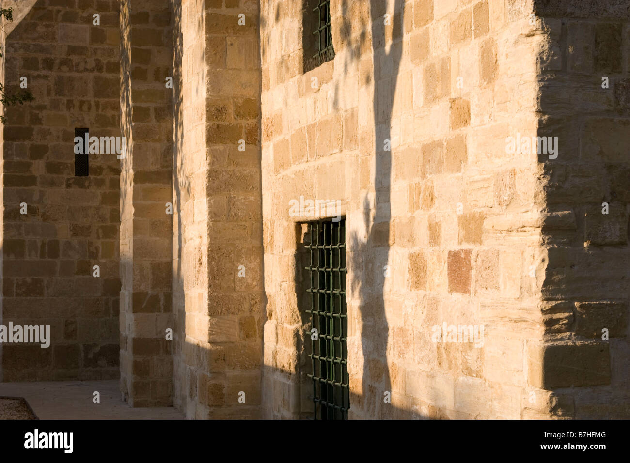 Hala Sultan Tekkesi mosque details of yellow stone wall and window bars with beautiful tree shadow on it. Larnaca, Cyprus Stock Photo