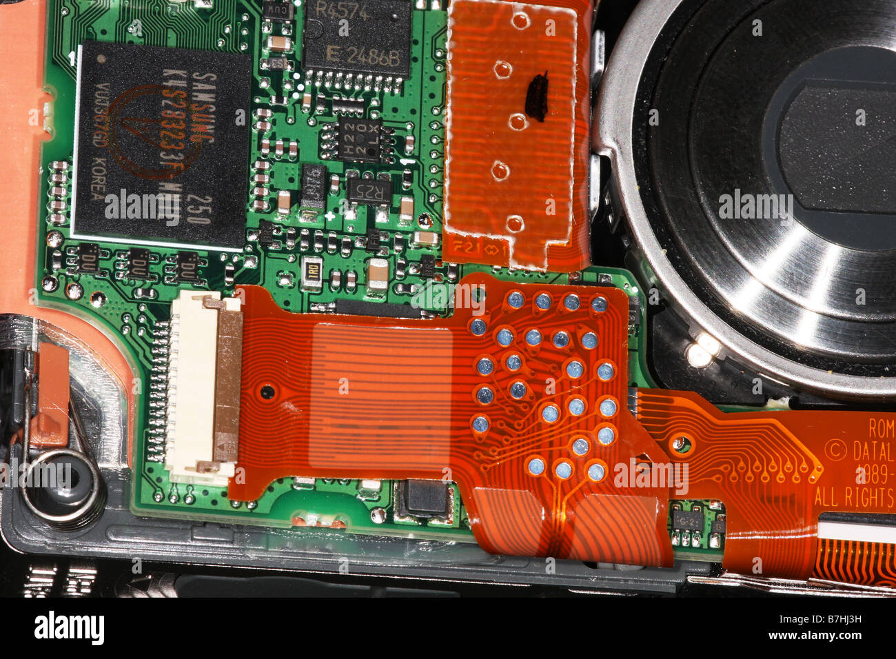 Part of the main circuit board in a digital camera with lens assembly on the right. Stock Photo