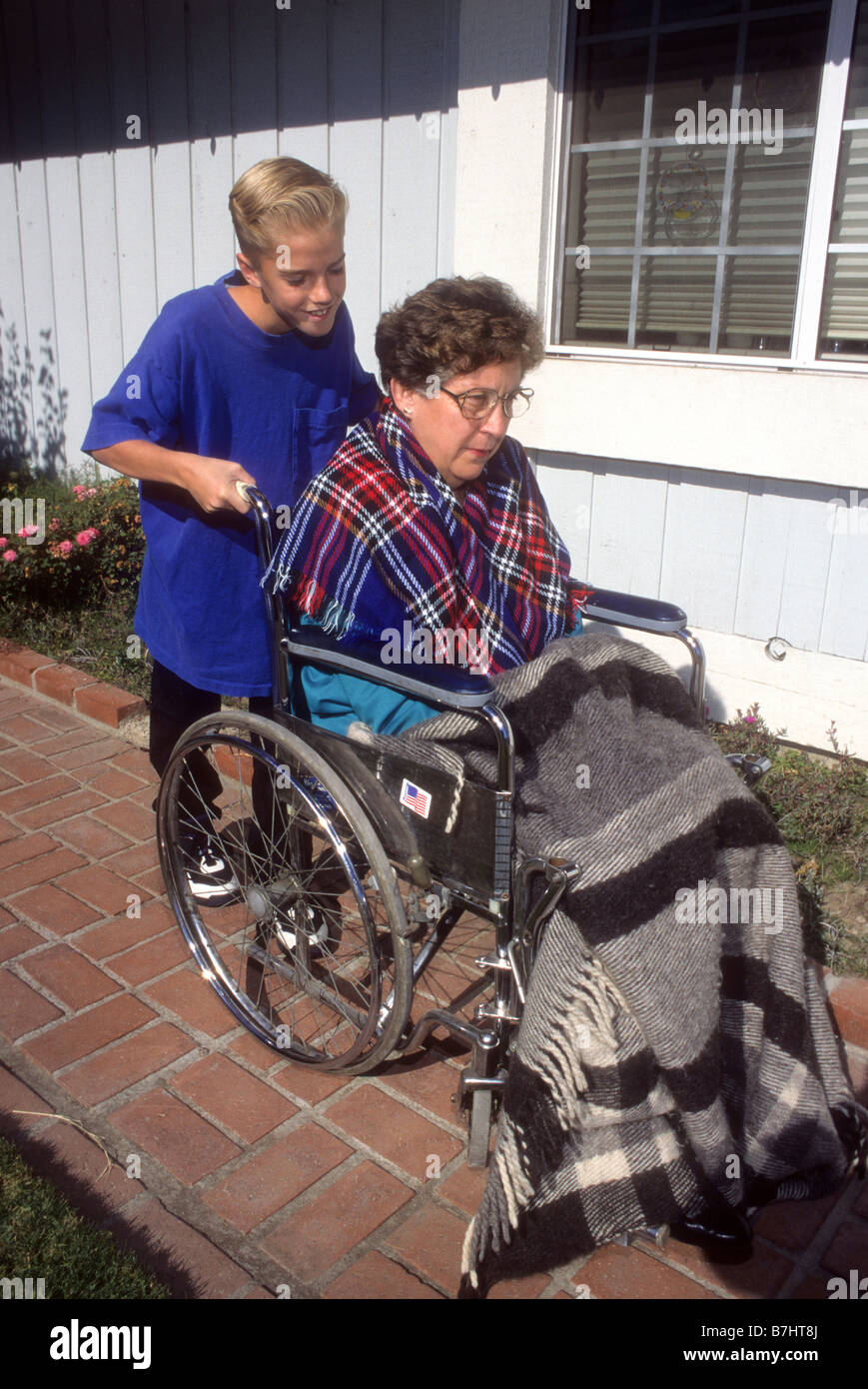 Preteen boy pushes grandmother in wheel chair Stock Photo