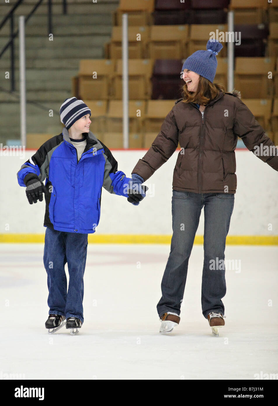 mother and son ice skating together indoors holding hands and smiling