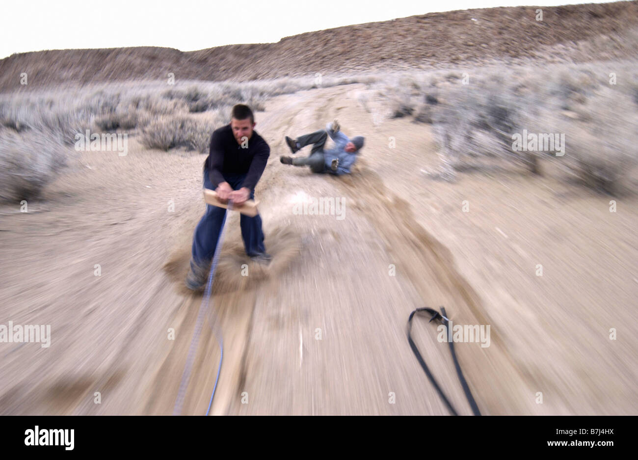 Two men (20-30) surfing behind a car on a dirt road, Bishop, California, USA Stock Photo