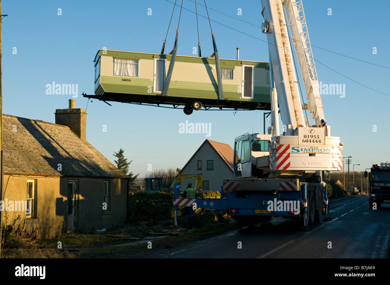 A crane lifting a mobile home over a cottage in the village of Mey