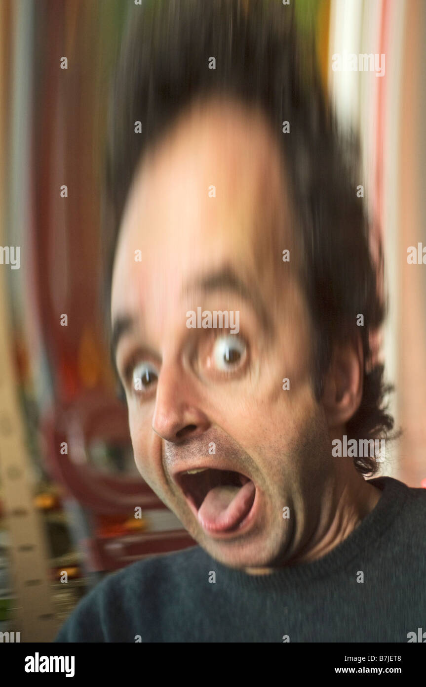 man pulling faces in a distorting mirror with wide eyes and tongue sticking out. Stock Photo