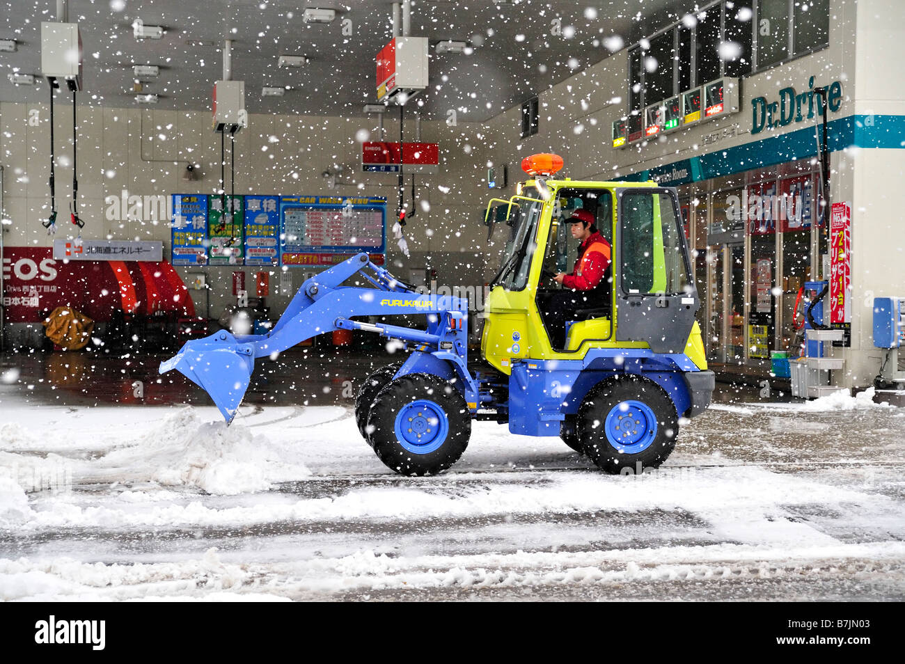 Employee of a Japanese gas station plowing snow with a small bulldozer
