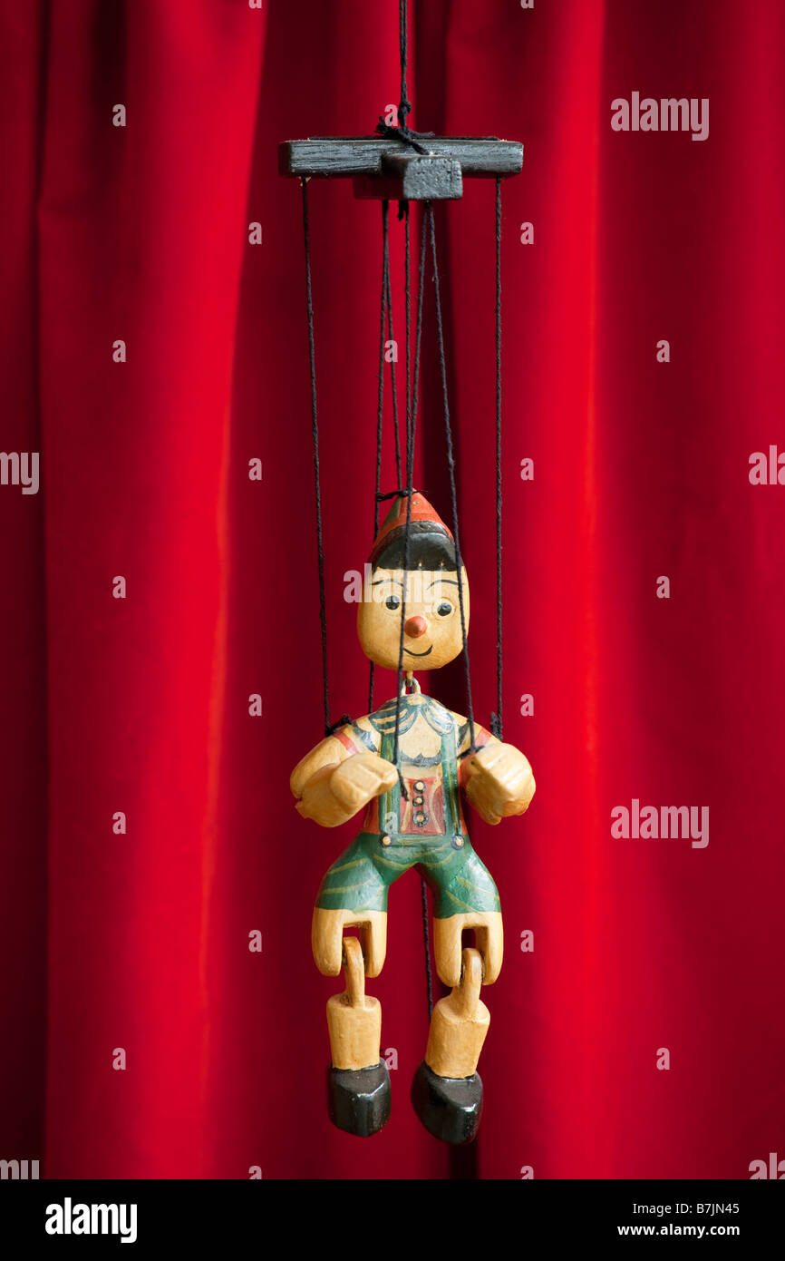 Pinocchio wooden marionette hangs in front of red curtain Stock Photo