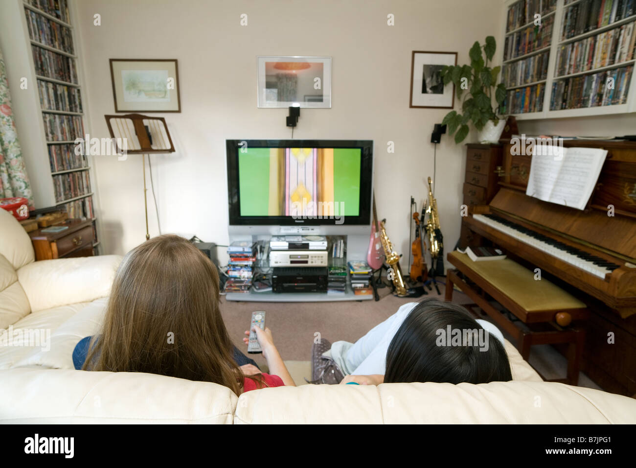 Rear view of two teenage girls watching a large TV indoors in the UK Stock Photo