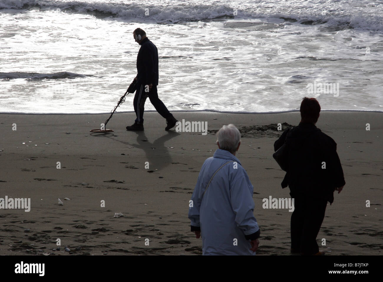 Women watching man on beach with metal detector Stock Photo - Alamy